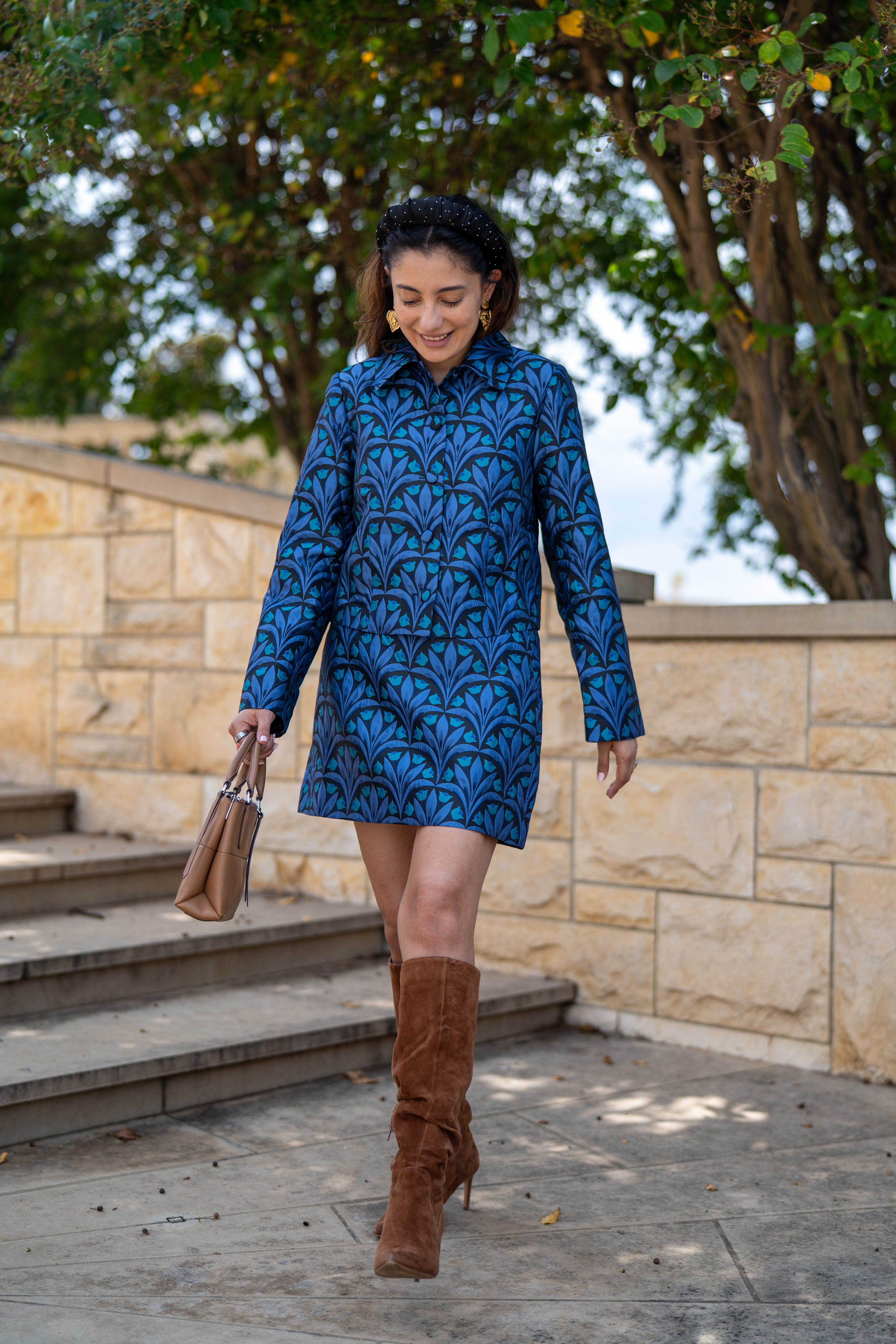 Woman in a blue patterned dress and brown boots walking outdoors.