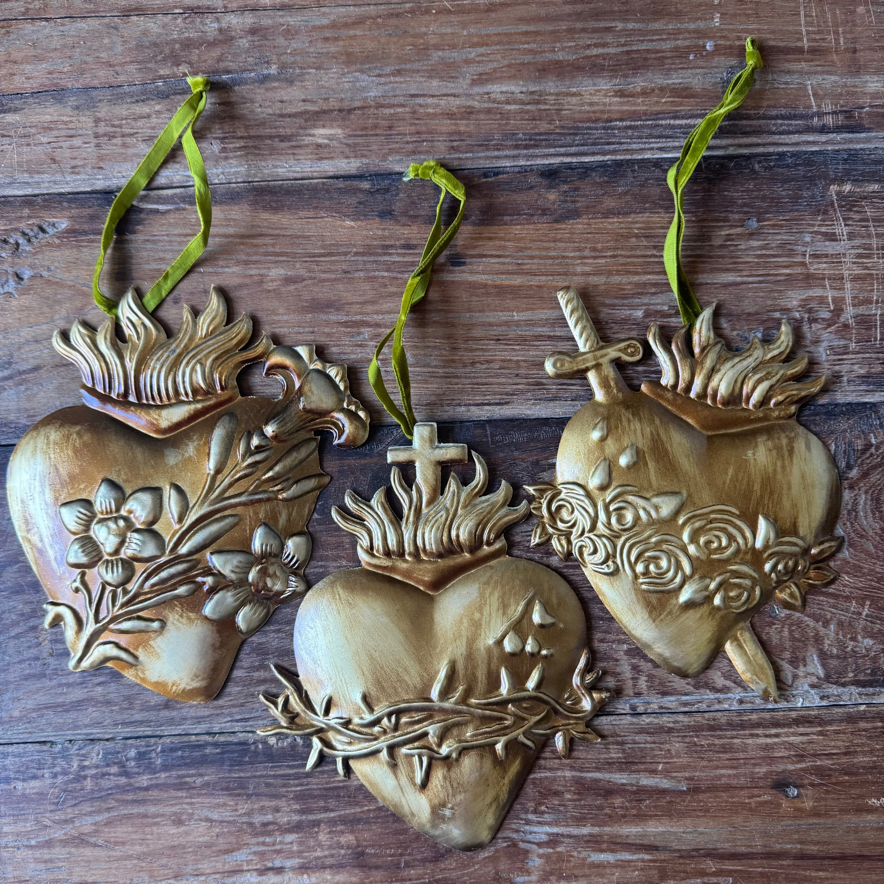 Three heart-shaped decorative items with floral and cross designs on a wooden surface.