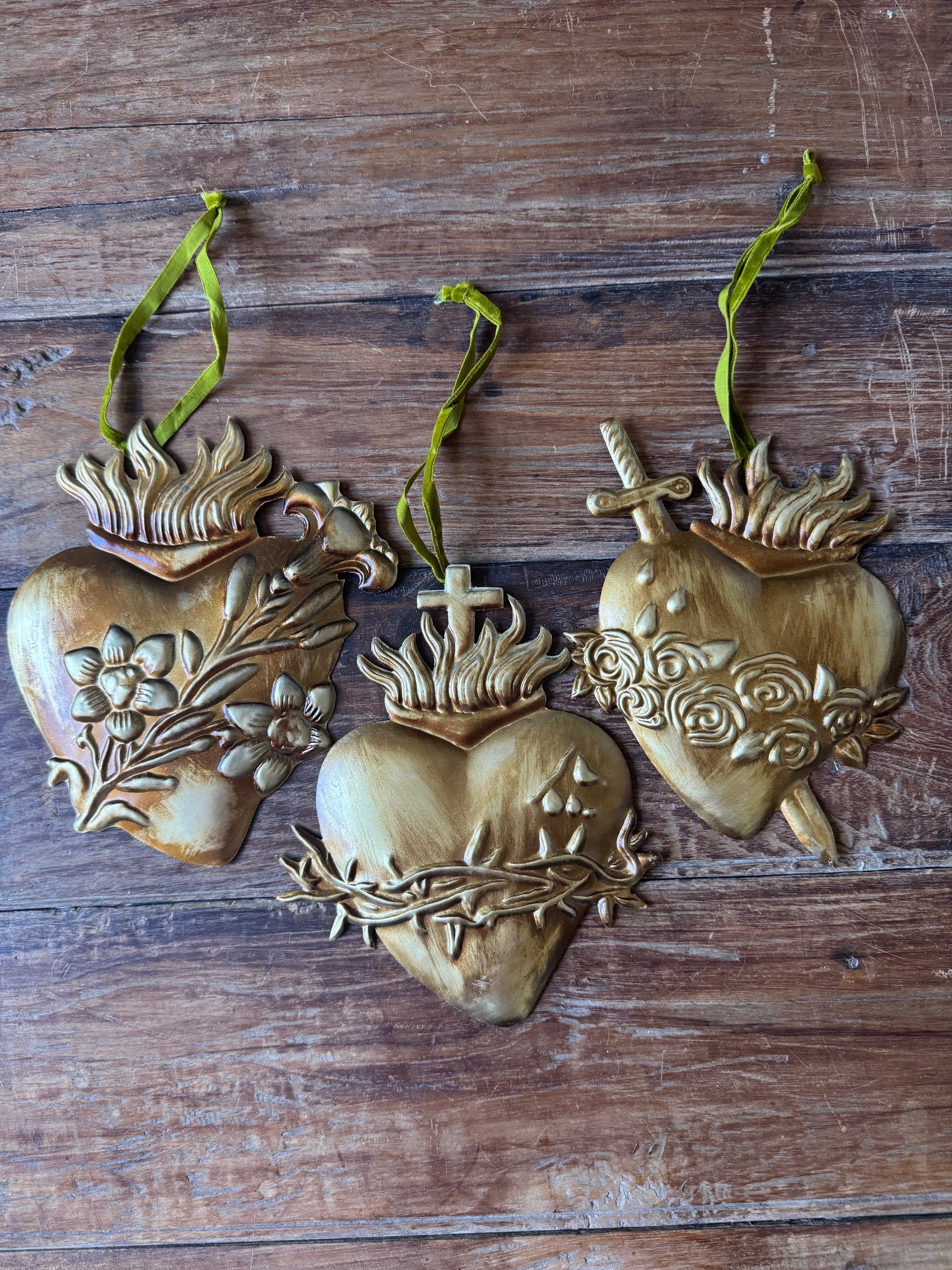Three heart-shaped decorative items with floral and cross designs on a wooden surface.